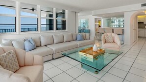 Una sala de estar moderna con una mesa de centro de vidrio, sofás color beige y grandes ventanales con vistas al mar.