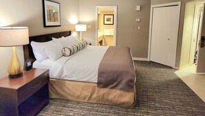 Habitación de hotel con cama, lámparas de noche, un cuadro en la pared, una puerta y suelo alfombrado.