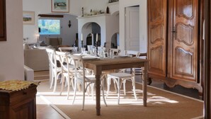 Un coin repas avec une table en bois et des chaises blanches, un grand meuble en bois et un lustre.