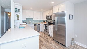 A modern kitchen with white cabinetry, stainless steel appliances, and a central island. - Newly renovated 2 bedroom, 2 bath condo with beautiful views of the ocean! (Ocean City)