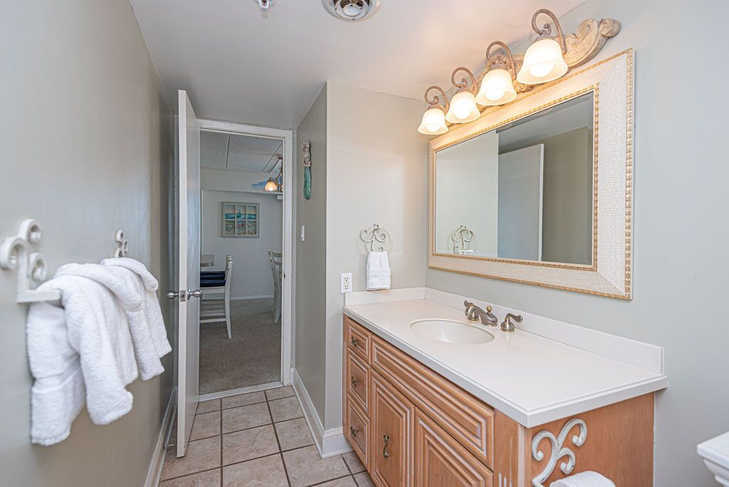 A bathroom with a white sink, wooden vanity, and a large mirror with lights.