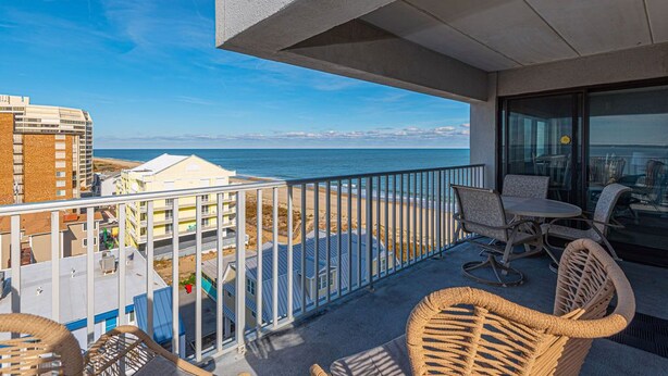 Un balcone con sedie in vimini, un tavolo e vista sulla spiaggia e sull'oceano.