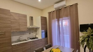 A modern kitchen with wooden cabinets, a built-in stove, and a dining area with a table set for two. - La Perla Apartment (Sant'Agnello)