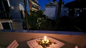 An outdoor patio with a table and chairs, a lit candle, and a view of buildings and trees in the background. - La Perla Apartment (Sant'Agnello)