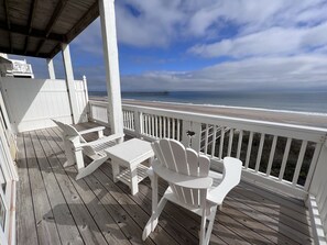 Een houten terras met witte meubels, met uitzicht op een strand en een pier.