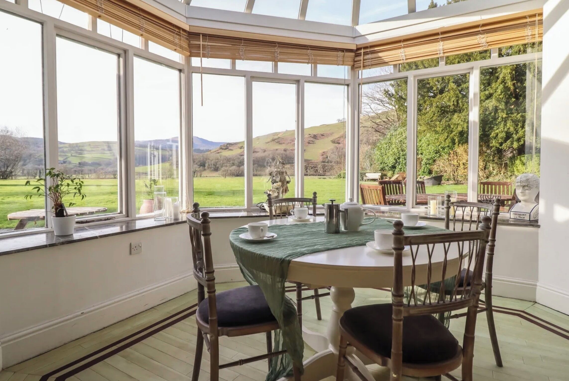 A conservatory with a table set for two, overlooking a rural landscape.
