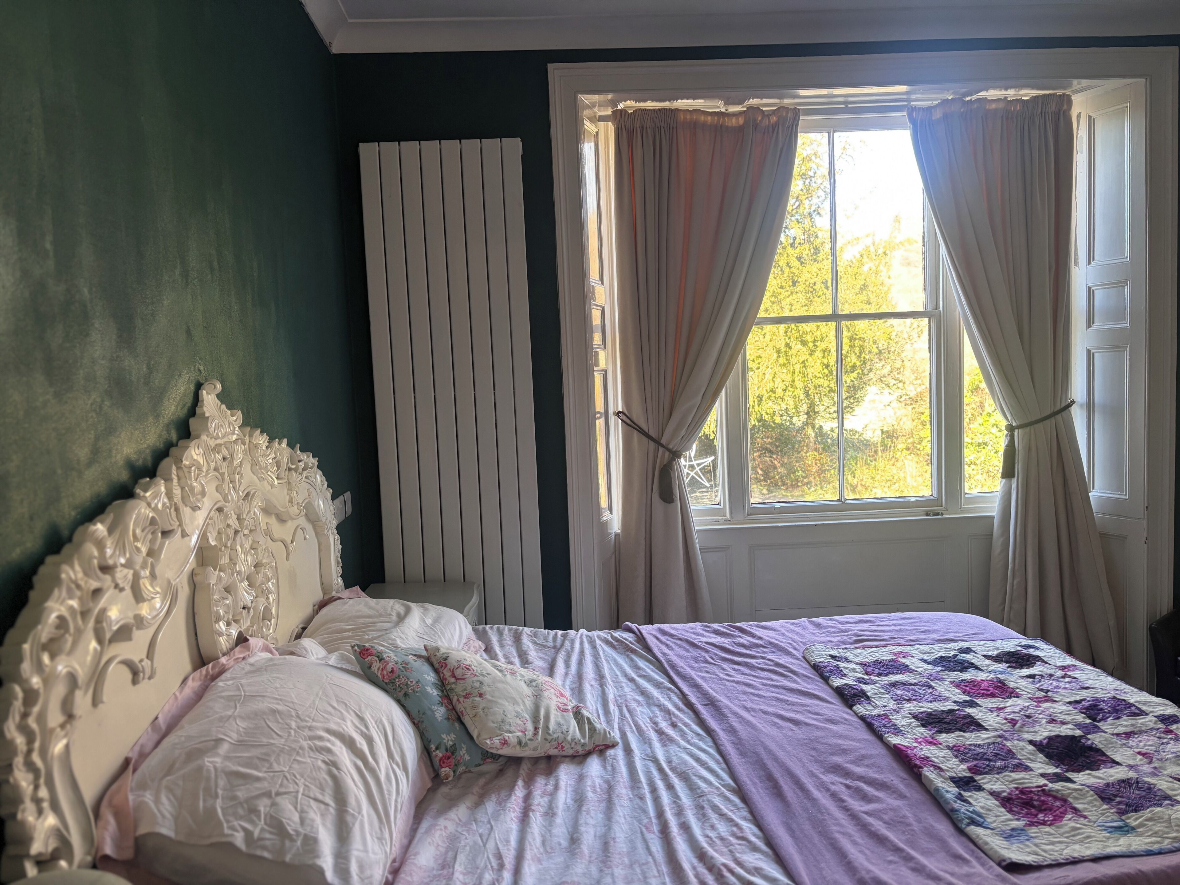 A bedroom with a bed, a window with curtains, and a radiator.