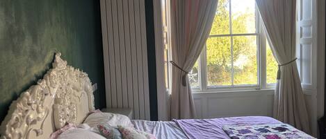 A bedroom with a bed, a window with curtains, and a radiator.