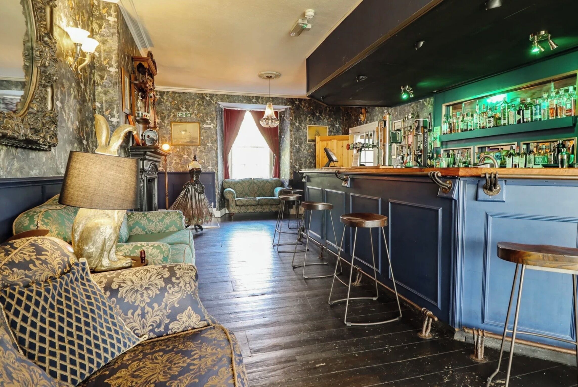 A bar area with a bar counter, stools, and a variety of bottles.