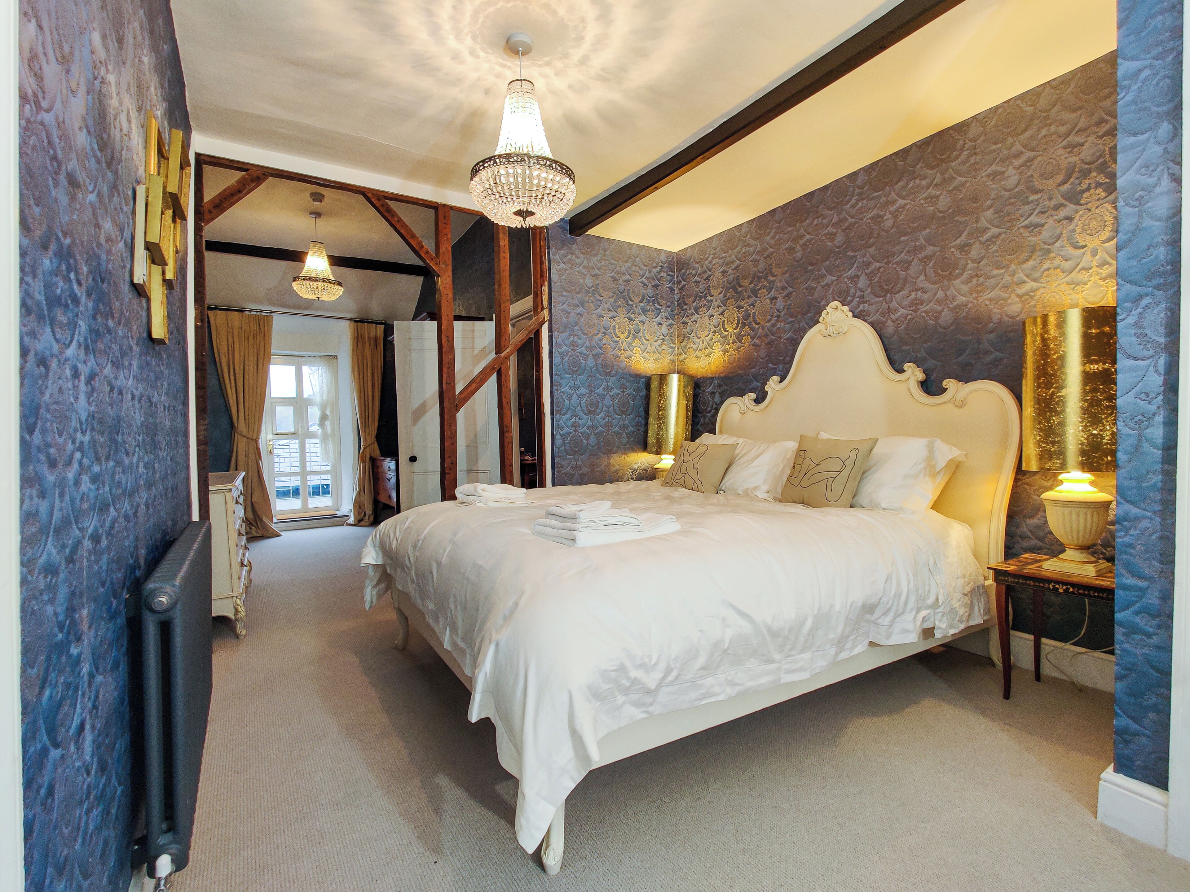 A spacious bedroom with a large bed, a chandelier, and a view of the outdoors.