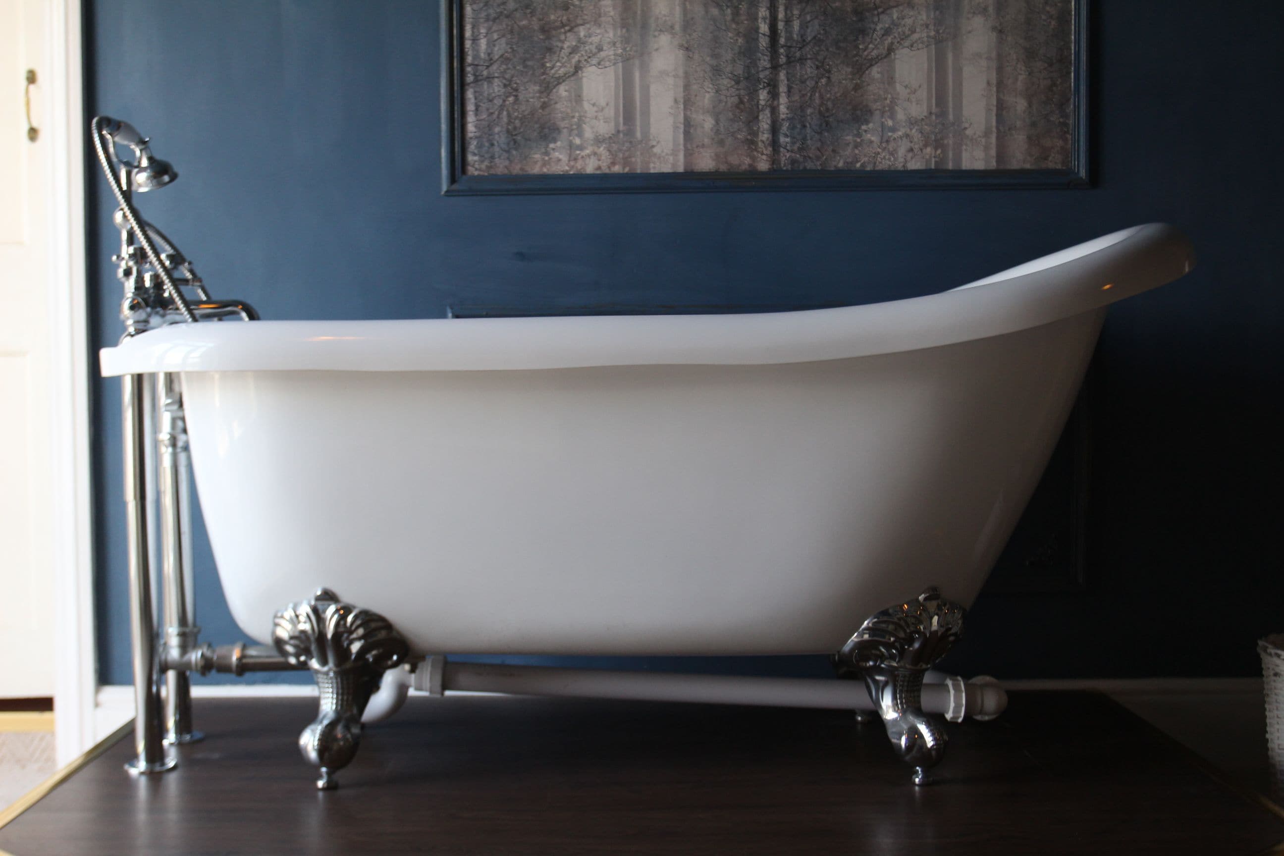 A freestanding bathtub with ornate legs, a white interior, and a blue wall with a framed picture above it.