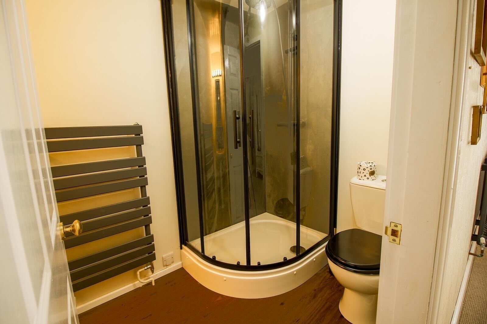 A shower enclosure with a glass door, a toilet, and a radiator.