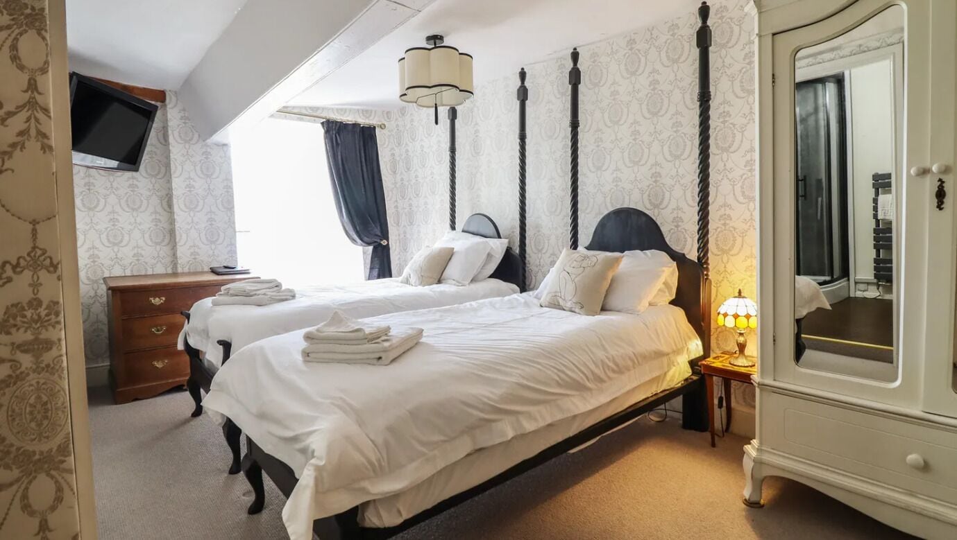 A hotel room with two beds, a wardrobe, a television, and a lamp.