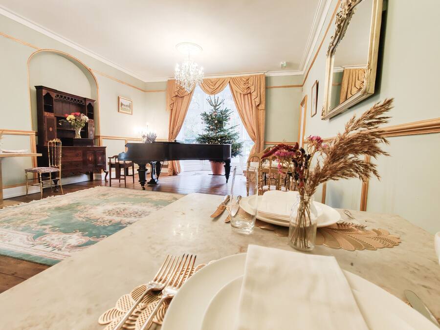 Un comedor con un piano, un árbol de Navidad y una mesa preparada para una comida.