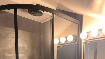 A glass-enclosed shower with a black frame, a sink with a mirror, and three bottles of shampoo.