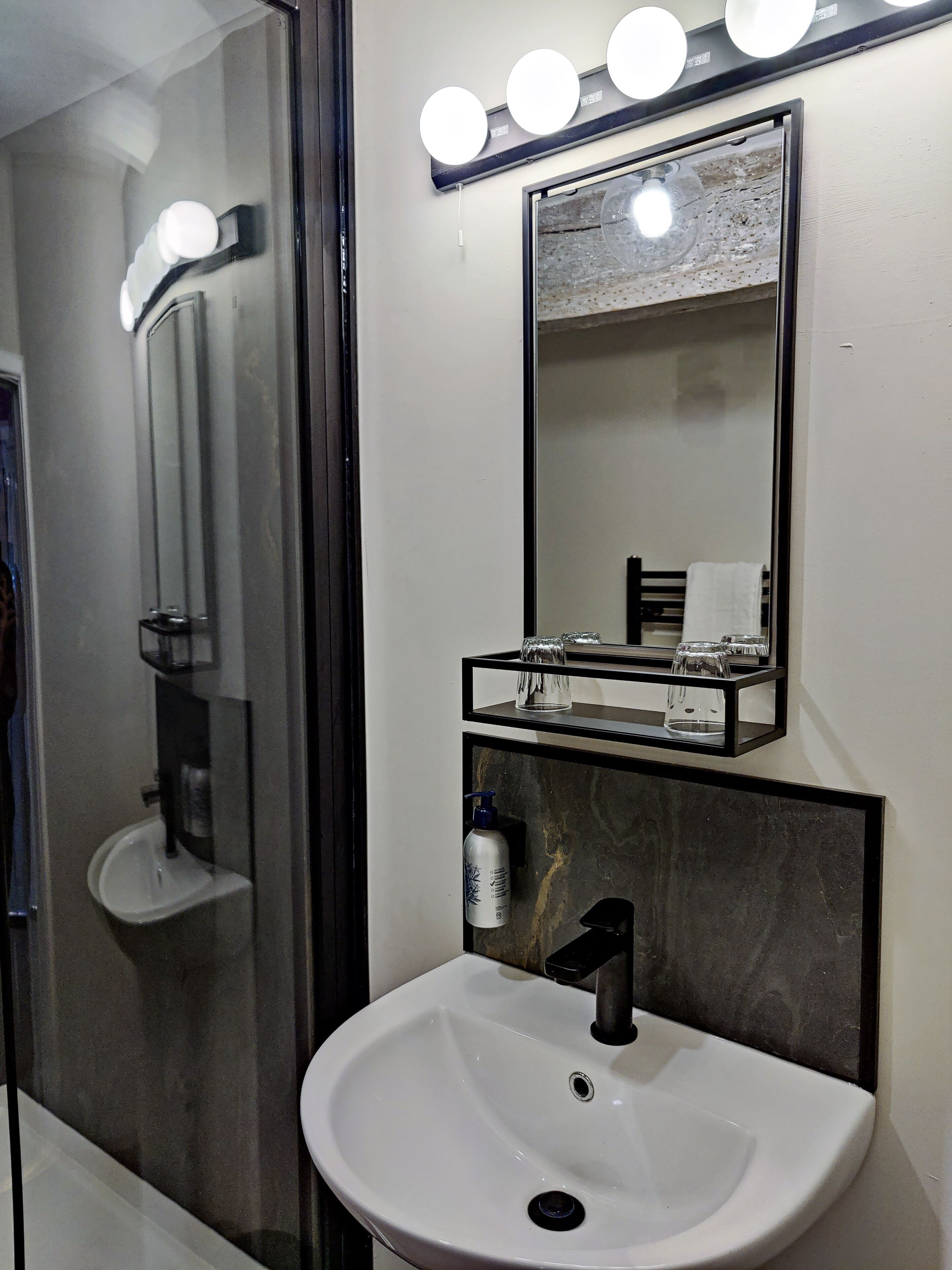 A bathroom with a white sink, a mirror with lights, and a glass shower enclosure.