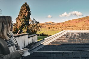 A person holding a cup on a rooftop with a view of a hilly landscape.