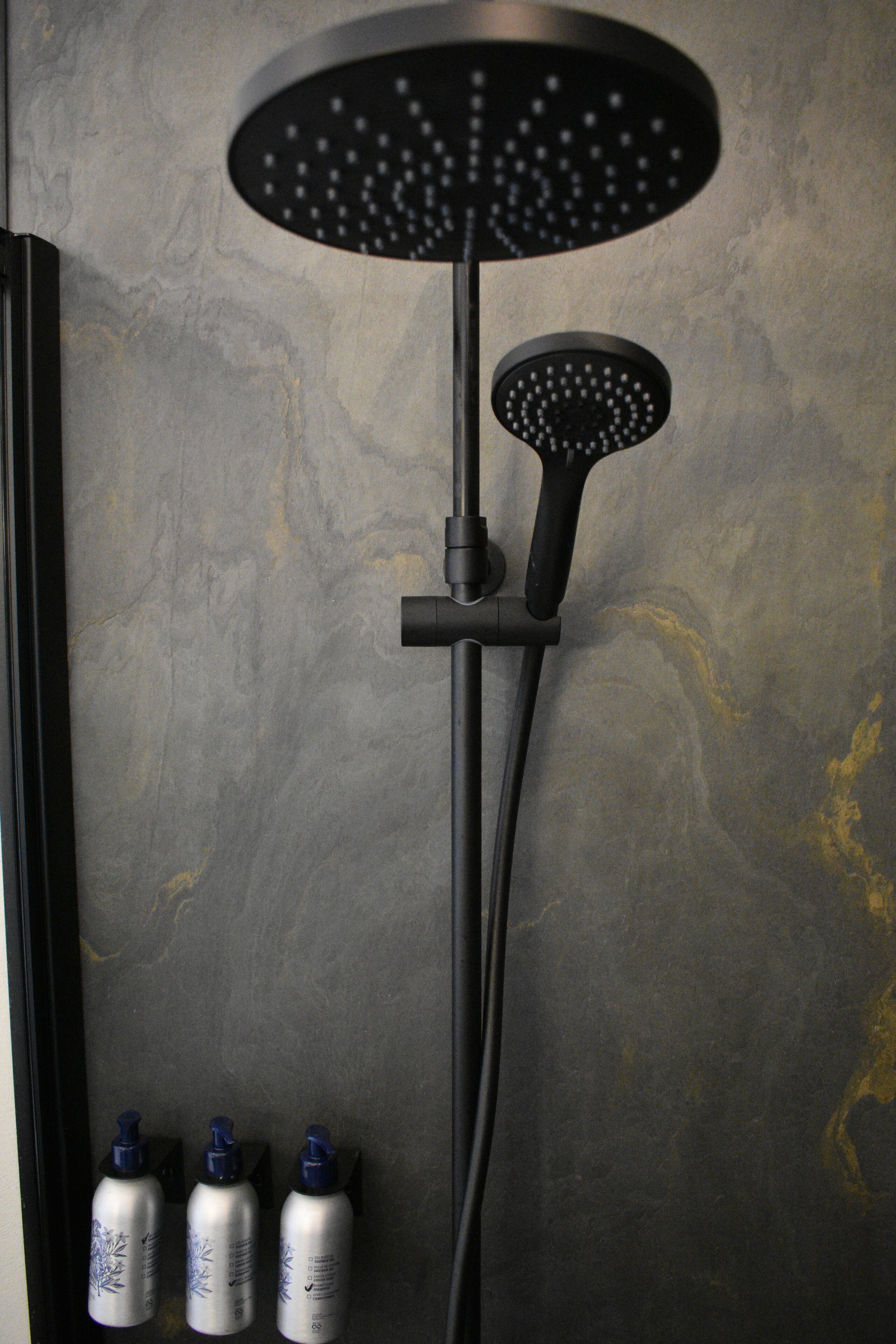 A modern shower with a circular head, a handheld showerhead, and three bottles of shampoo.