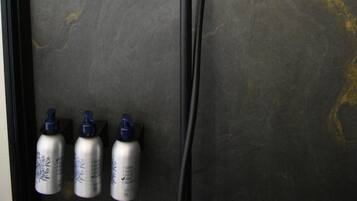 A modern shower with a circular head, a handheld showerhead, and three bottles of shampoo.