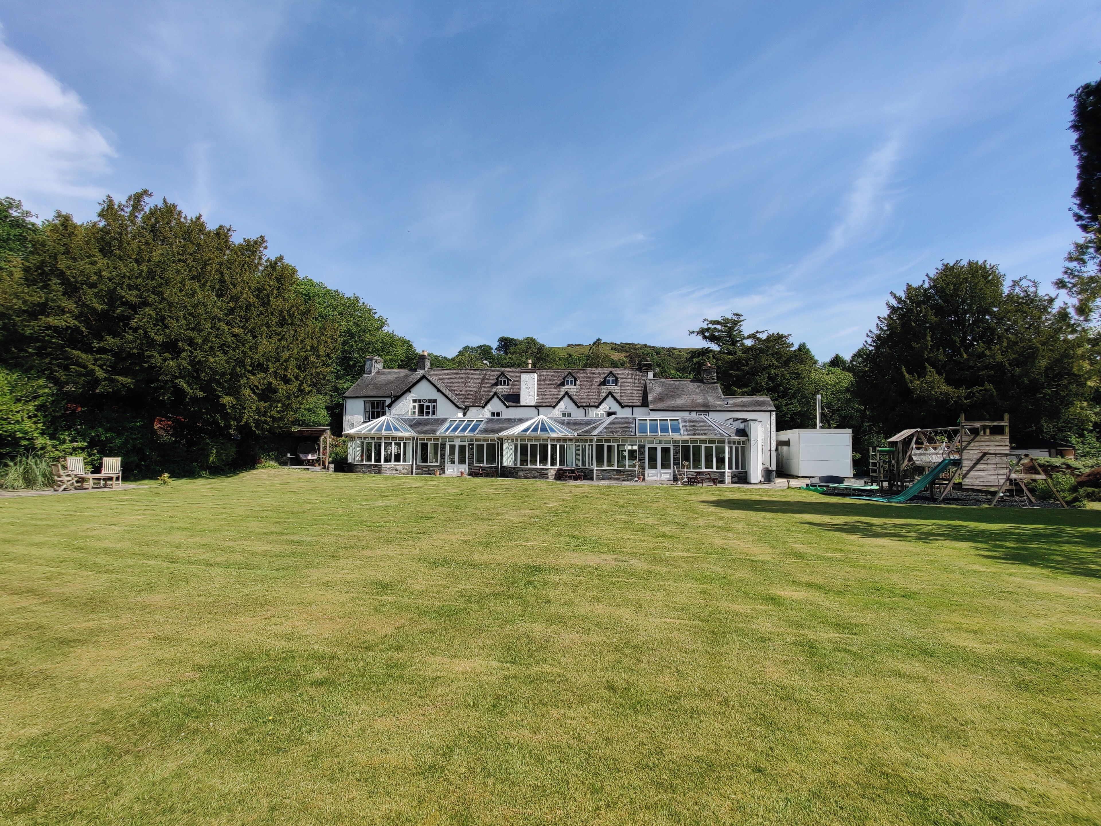 A large building with a lawn in front, a playground to the right, and trees in the background.