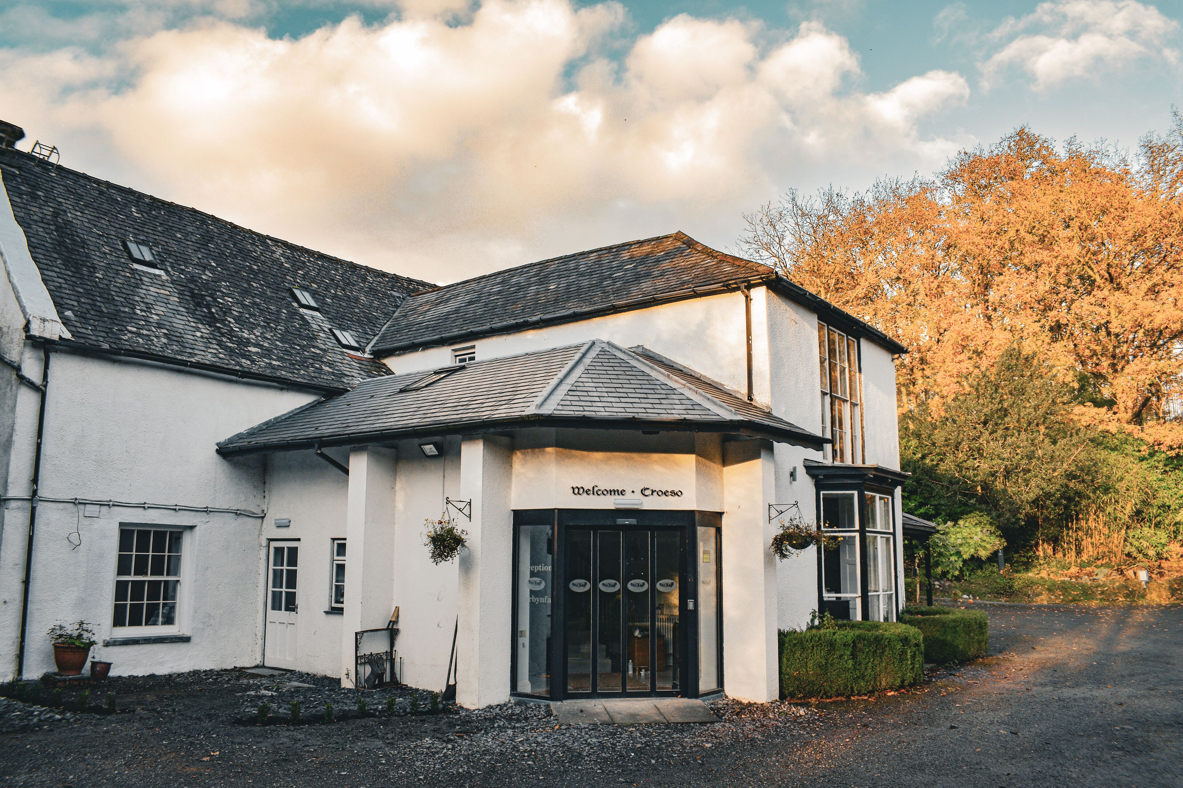 A white building with a black entrance, labeled "Welcome - Croeso," and a gravel driveway leading to it.