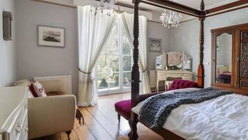 A four-poster bed with a canopy, a wooden desk with a mirror, and a view of the outdoors through a large window.