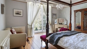Una cama con dosel y cortinas, un escritorio de madera con espejo, y vistas al exterior a través de un ventanal.