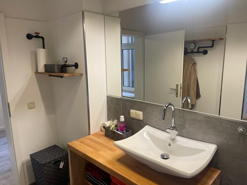A modern bathroom with a wooden vanity, a white sink, and a large mirror.