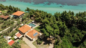 An aerial view of a residential area with multiple houses, a swimming pool, and dense forest.