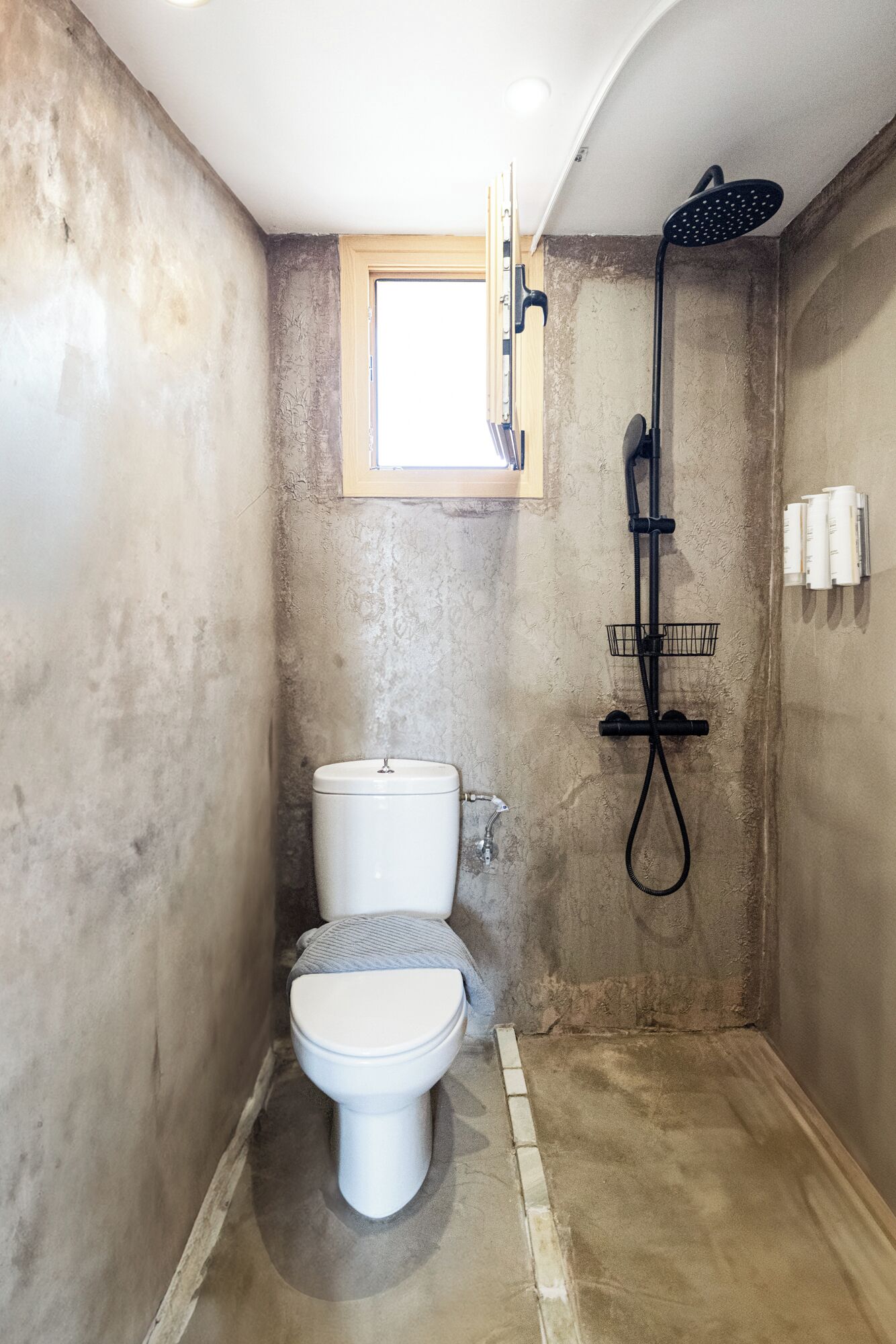 A compact bathroom with a toilet, a shower, and a small window.