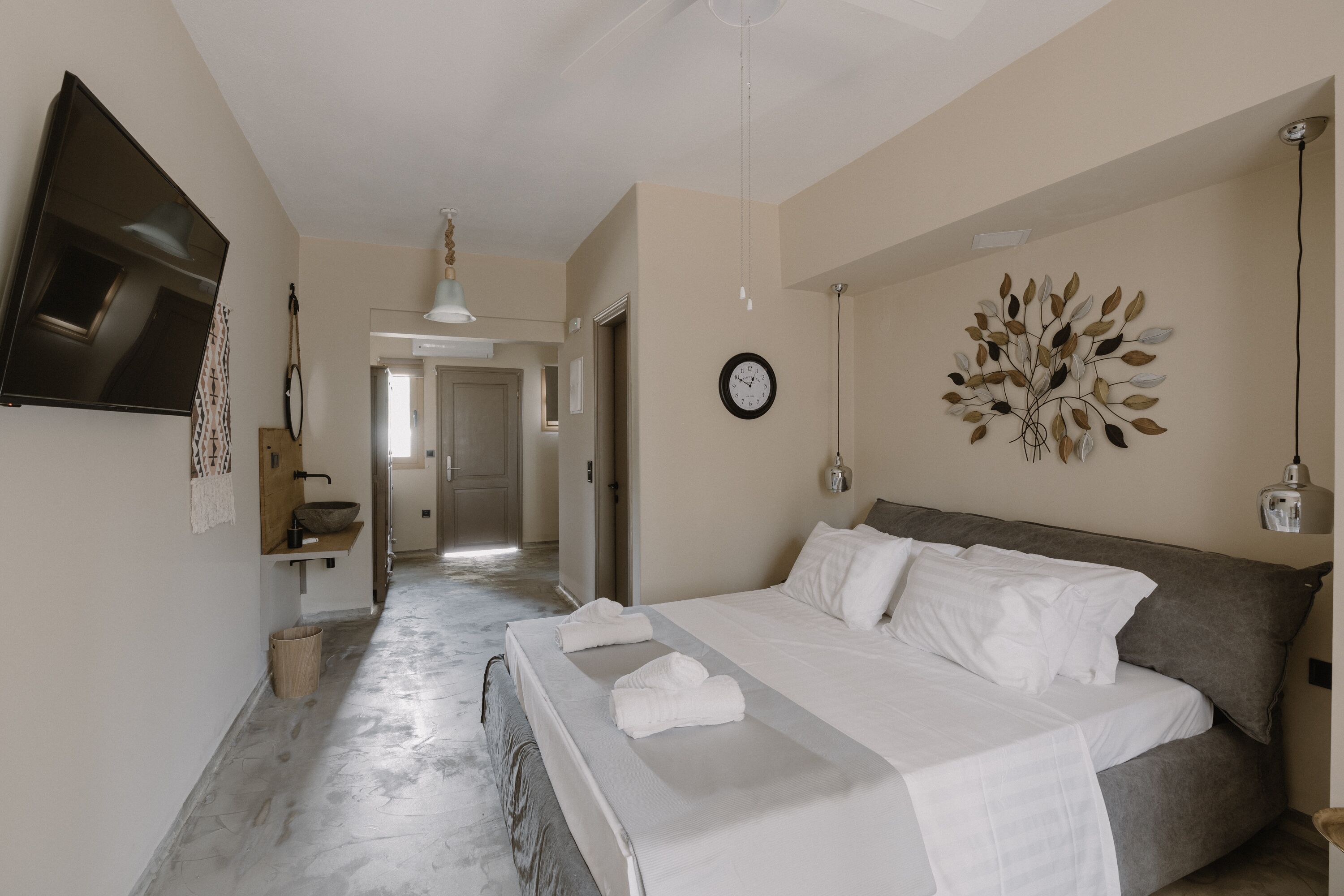 Une chambre d’hôtel avec un grand lit, un téléviseur à écran plat fixé au mur, une horloge et un élément décoratif mural.