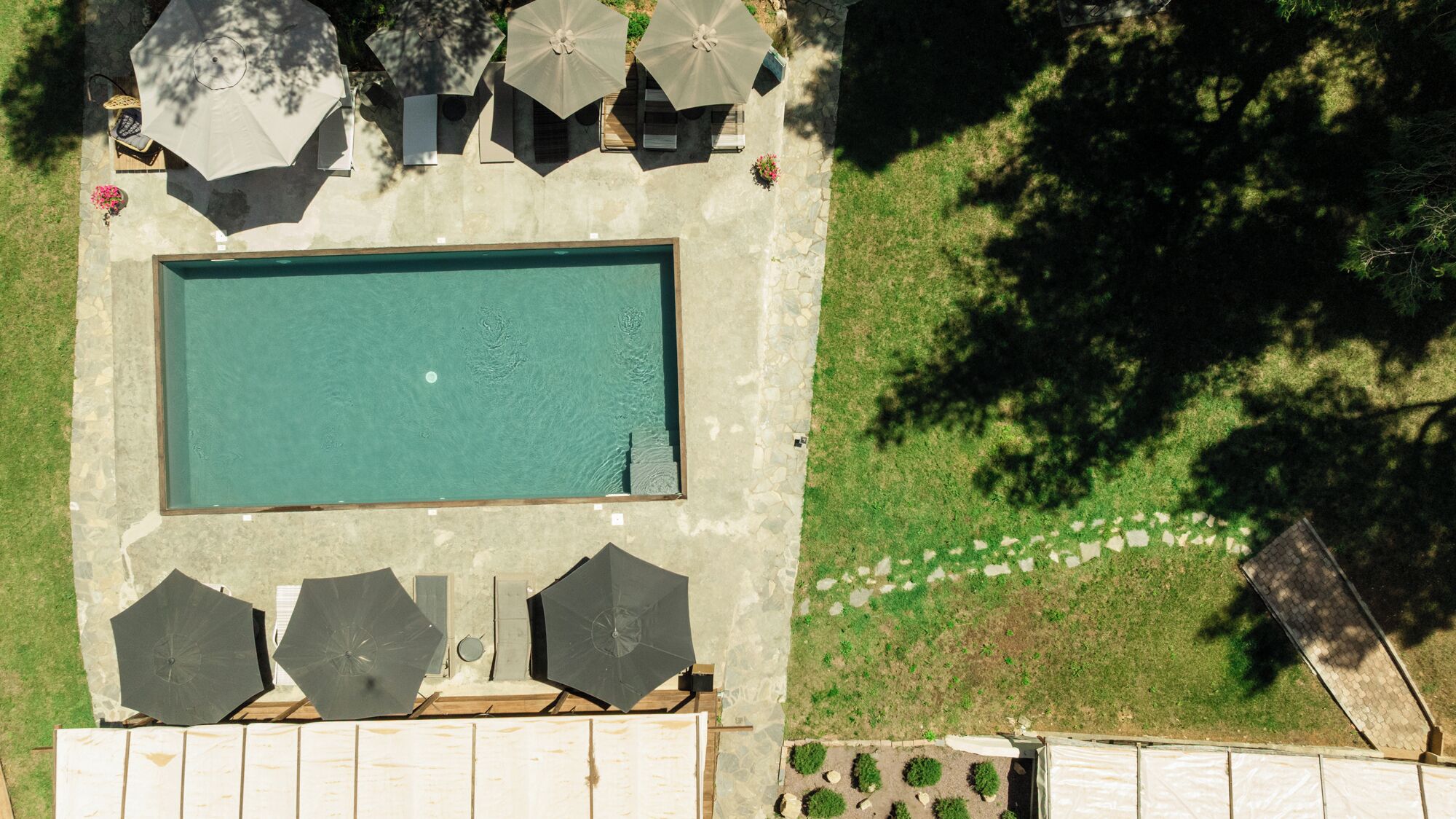 An aerial view of a swimming pool with surrounding umbrellas and a stone pathway.