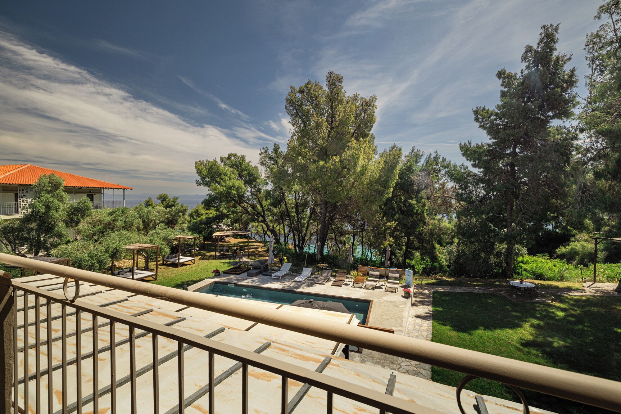 A pool area with lounge chairs and umbrellas, surrounded by trees and a view of the sea.