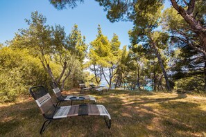 A serene outdoor seating area with metal chairs and tables, surrounded by trees and a clear view of the sky. - Pefkon Suites (Kassandra)