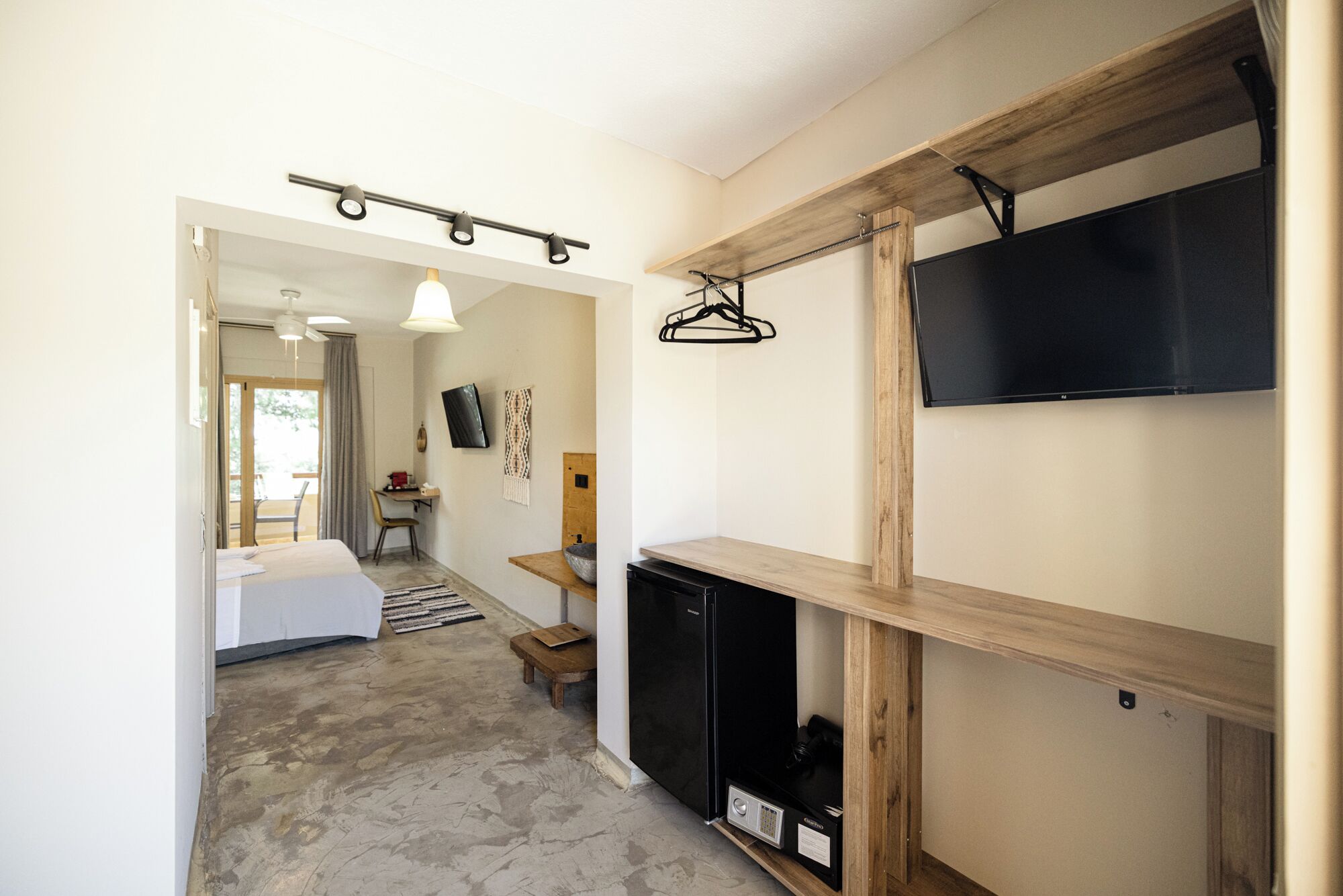 A modern hotel room with a large bed, a wooden cabinet, a television, and a desk with a chair.
