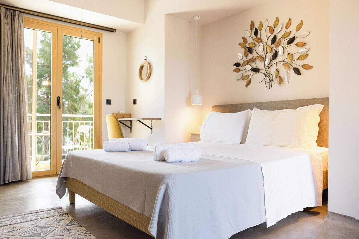 Une chambre dotée d’un grand lit, d’une tête de lit en bois, d’une lampe fixée au mur et offrant une vue sur l’extérieur grâce à une porte coulissante.
