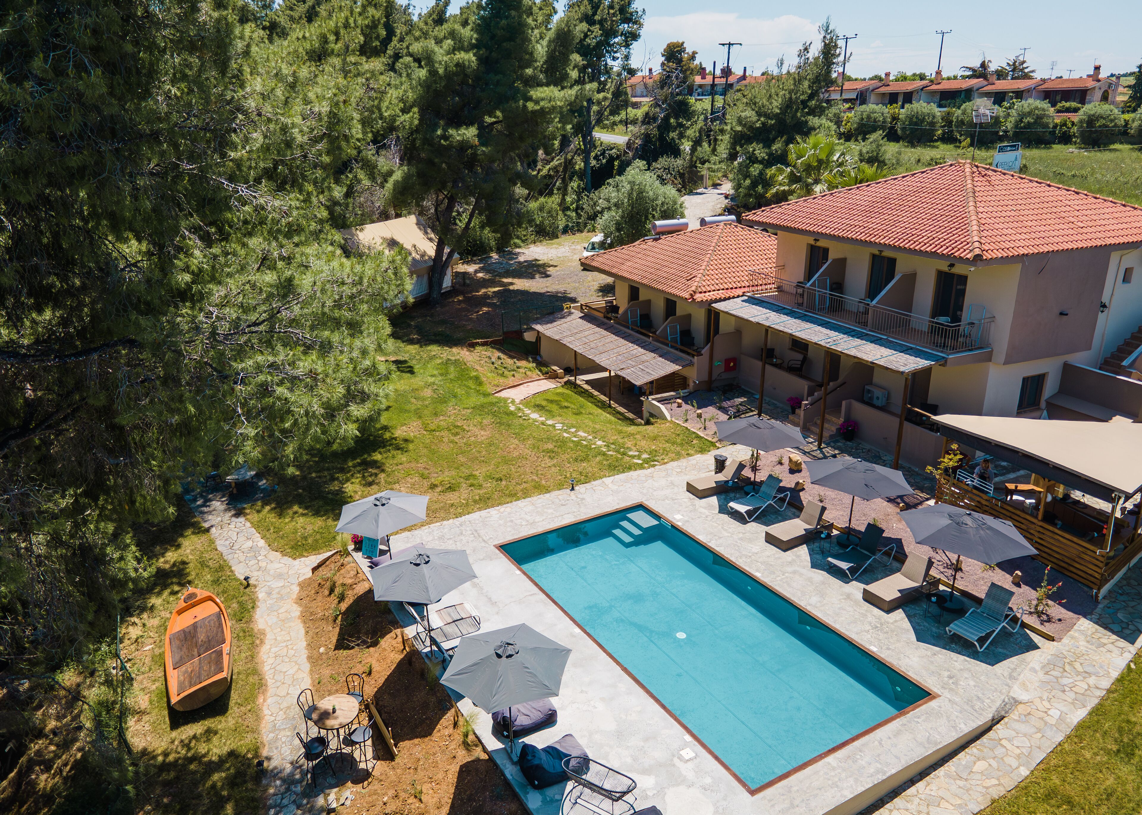 Una gran piscina con tumbonas y sombrillas, rodeada por un amplio patio y una casa grande con techo de tejas rojas.