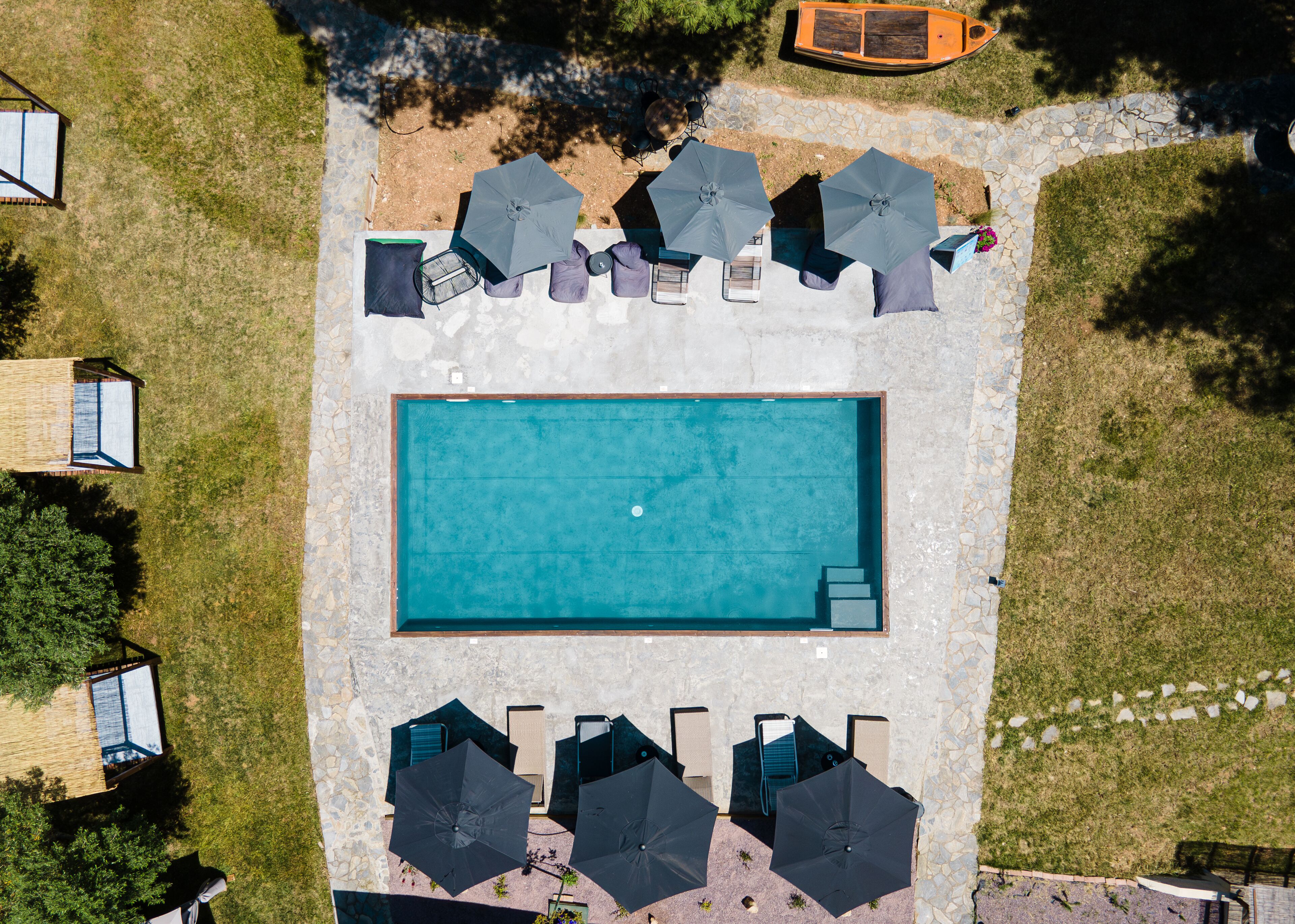 An aerial view of a swimming pool area with lounge chairs and umbrellas, surrounded by stone walls and greenery.