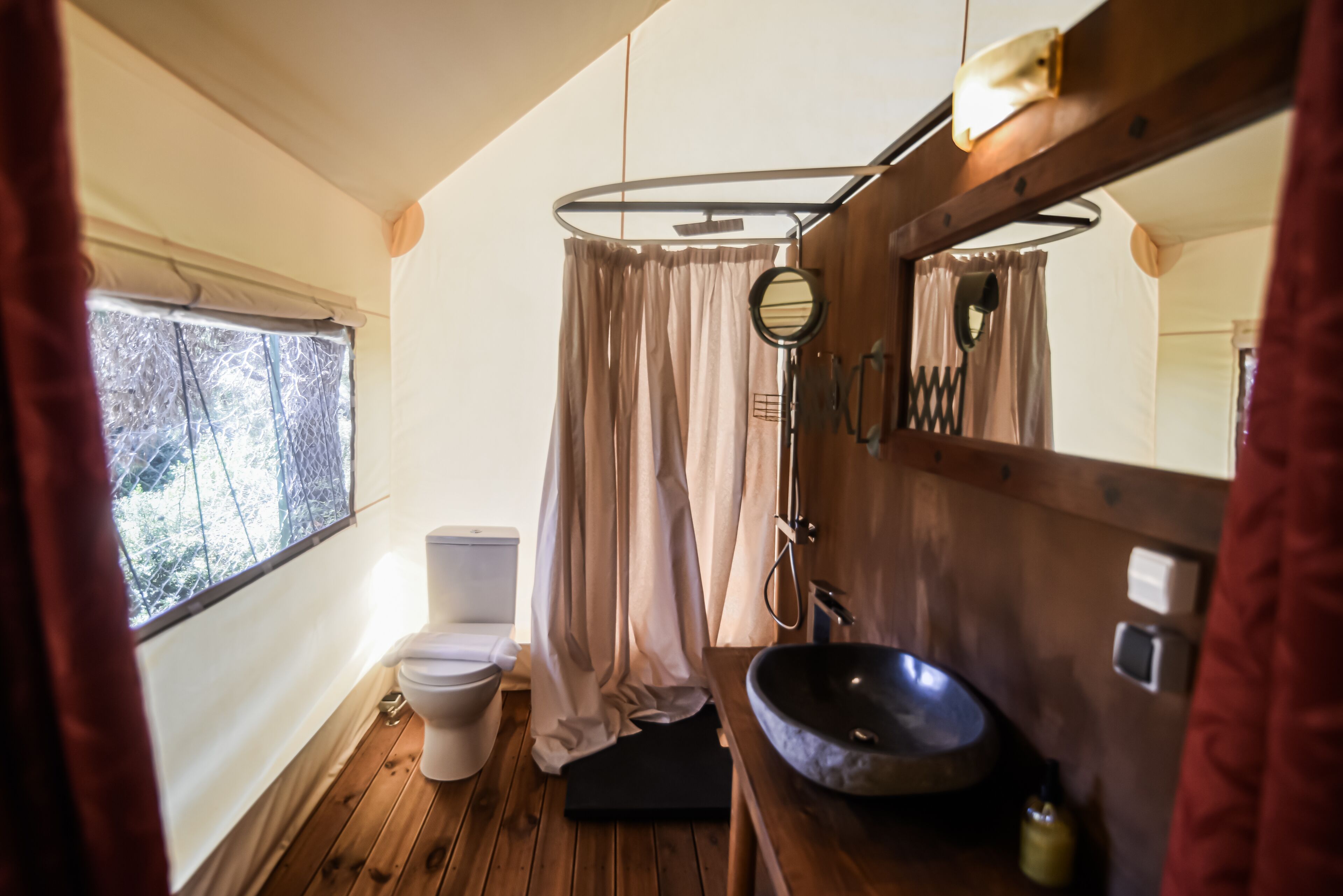 Un baño pequeño con suelo de madera, inodoro blanco, lavabo y zona de ducha con cortinas.