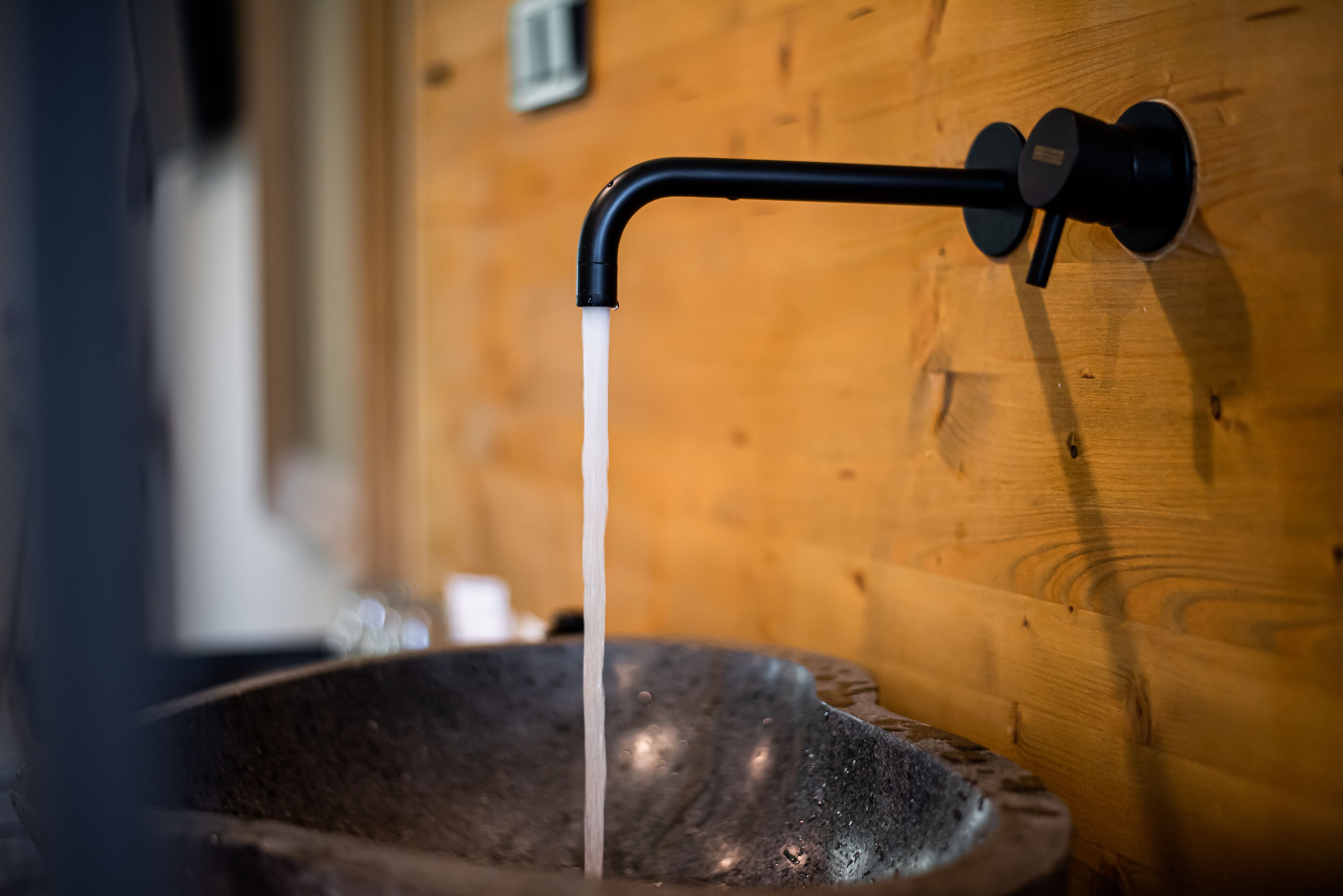 A stone basin with a black faucet against a wooden wall.