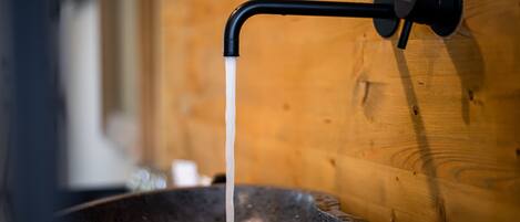 A stone basin with a black faucet against a wooden wall.
