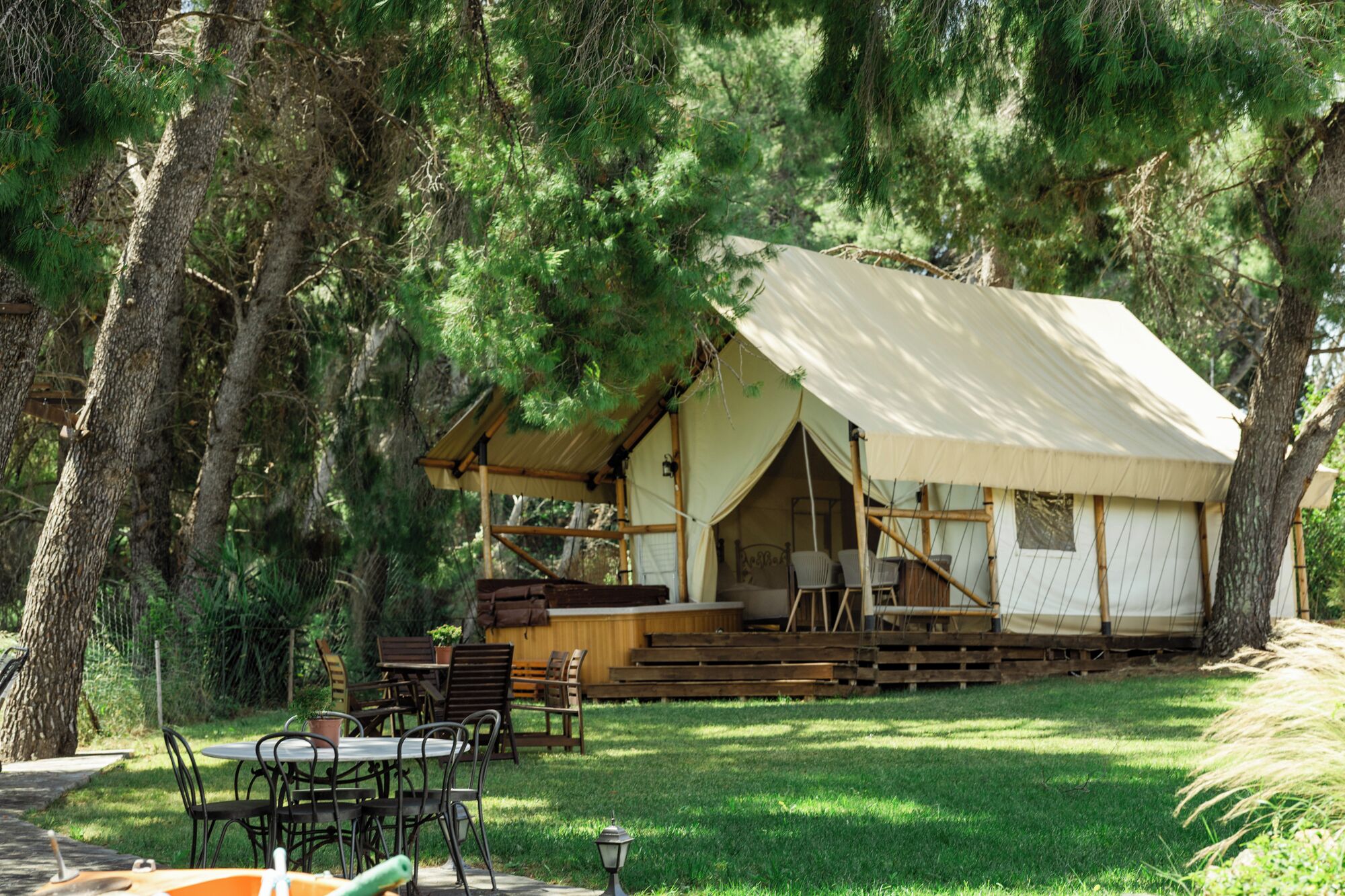 A rustic cabin with a covered porch, wooden furniture, and a lawn.