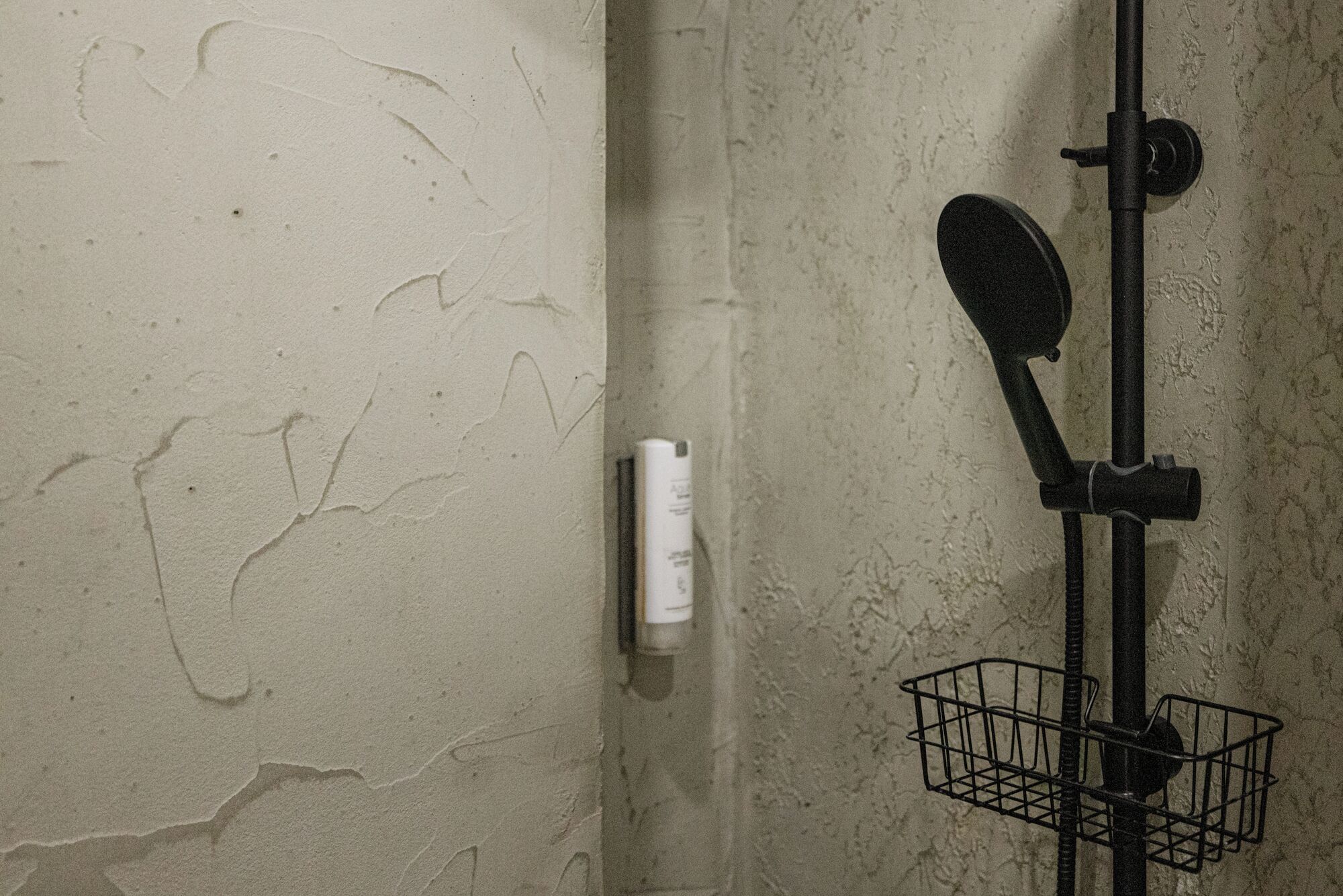 Een badkamer met een gestructureerde muur, een witte fles op de muur en een zwarte handdoekhouder met mand.