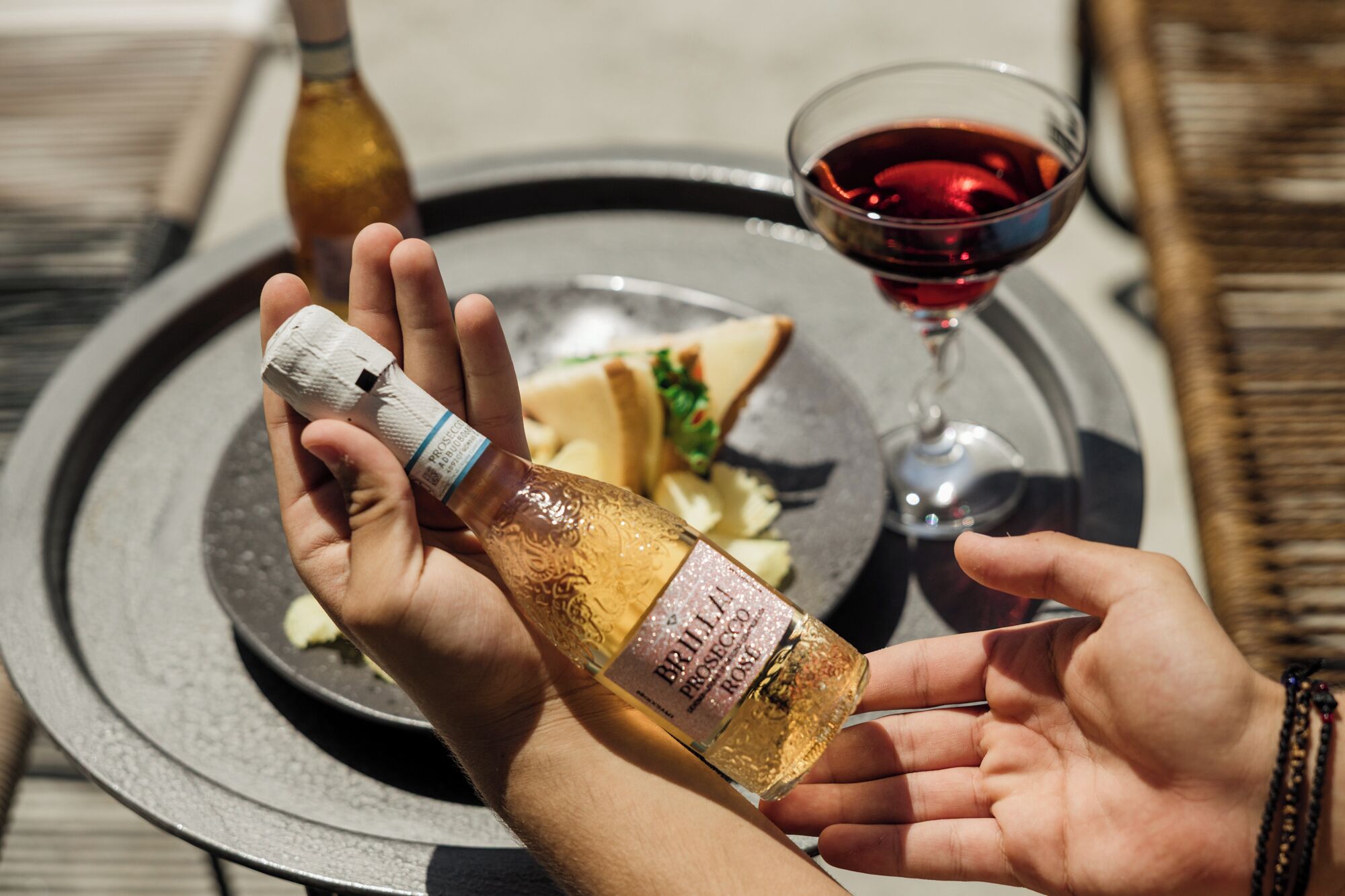A bottle of Brilla Prosecco Rosso wine being held by a person, with a glass of red wine and a plate with food in the background.