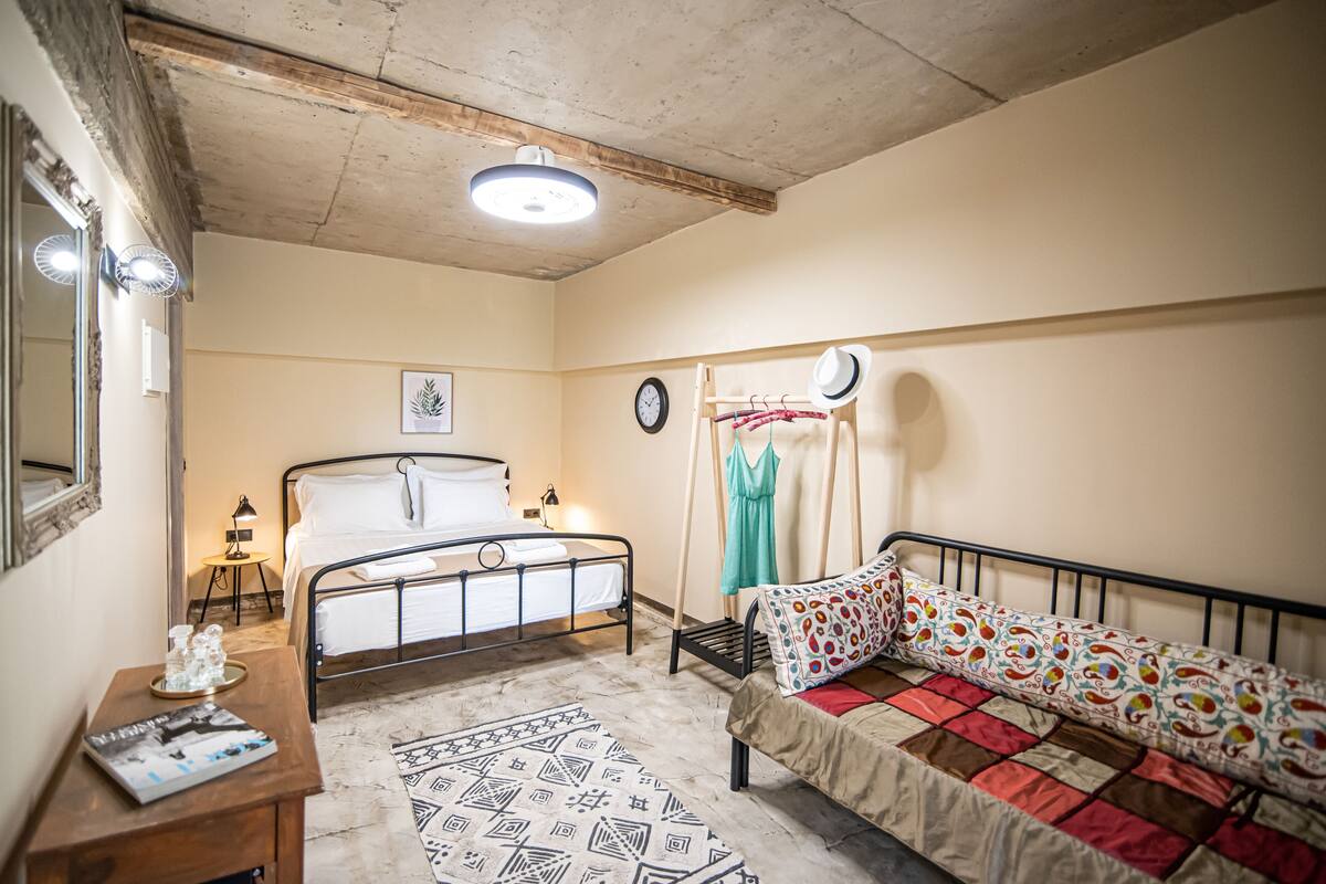 Une chambre à coucher avec un lit, un canapé, une petite table avec un magazine, une horloge murale et un miroir.