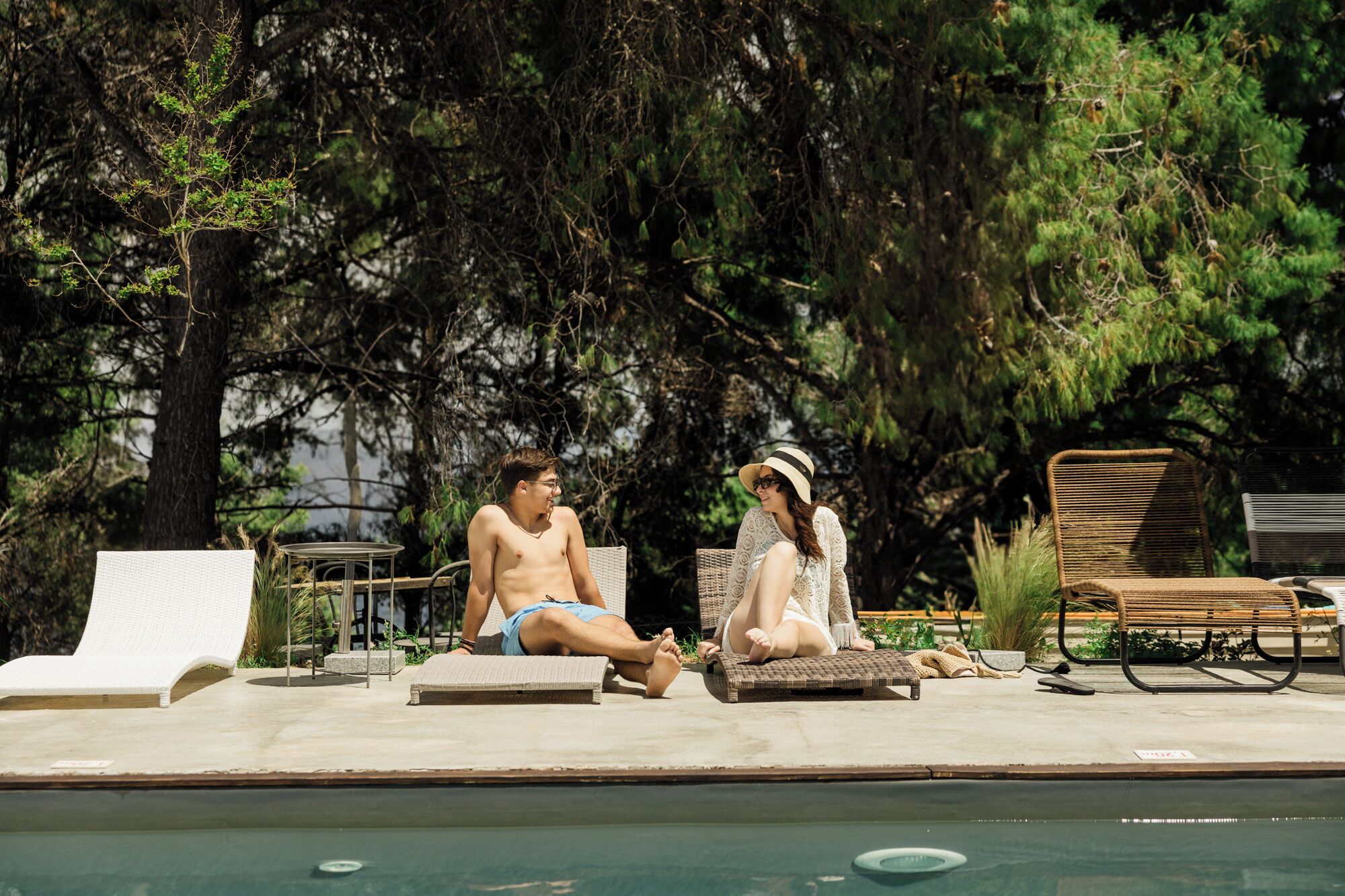 Un área junto a la piscina con sillones de descanso y un banco de madera.
