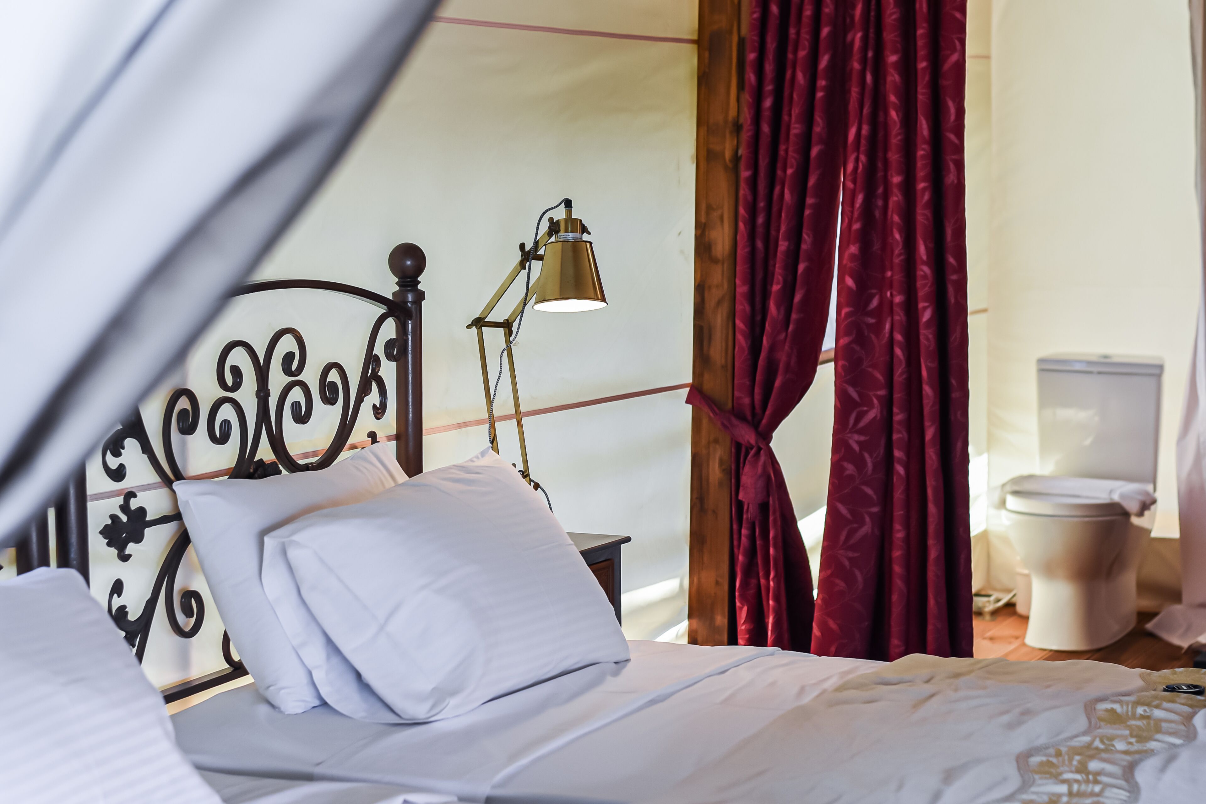 A neatly made bed with white linens and a gold lamp beside it.