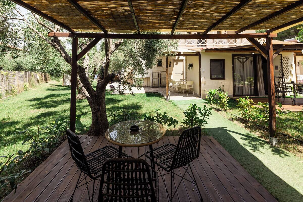 Une terrasse en bois avec une table et des chaises, entourée d’un jardin agrémenté d’une pergola.