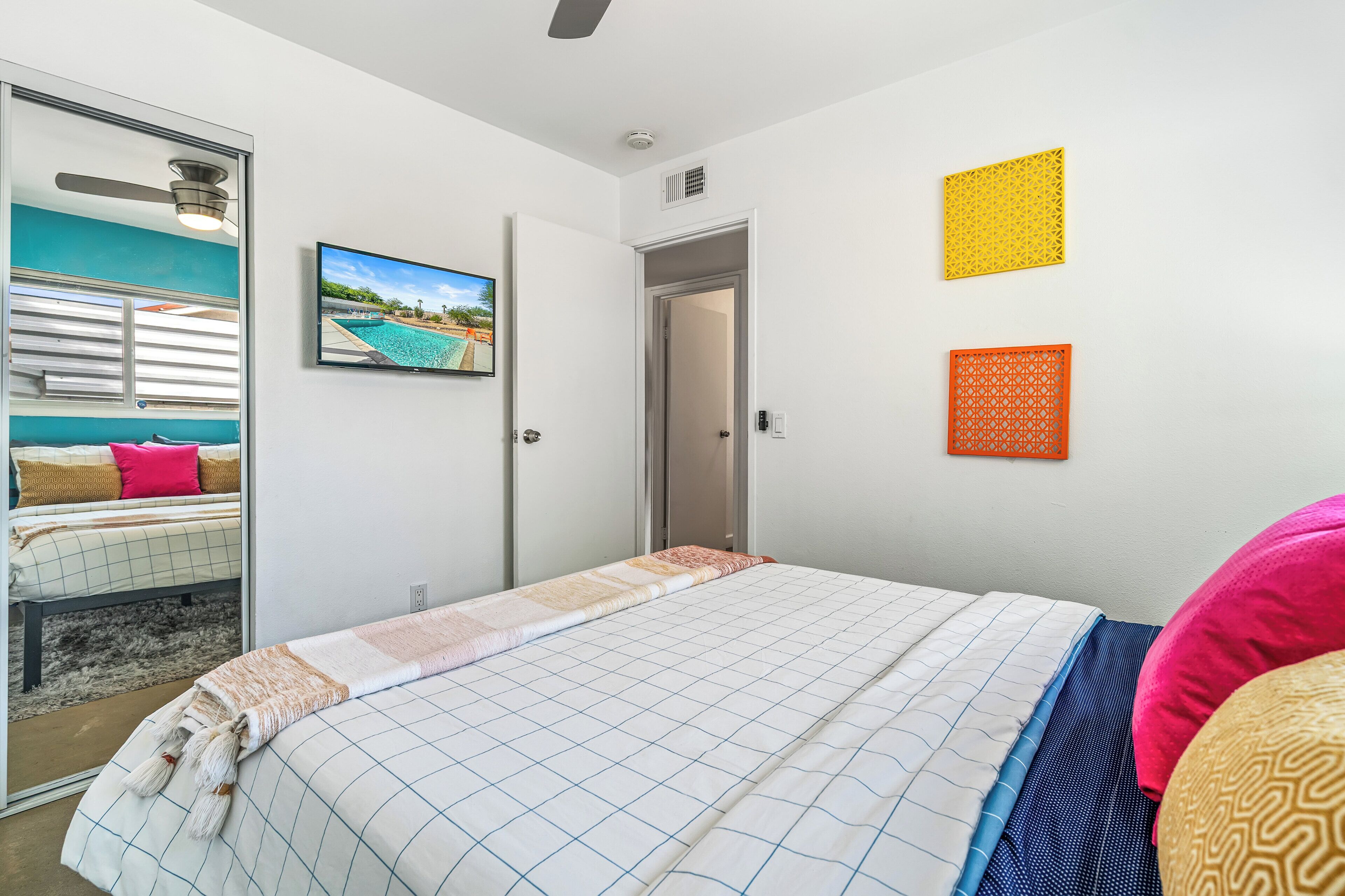 A bedroom with a bed, a door, a window, and a wall-mounted picture.