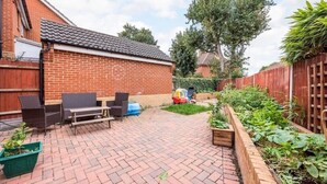 A brick patio with outdoor furniture, a garden bed, and a wooden fence. - The Lake Hub (Dagenham)